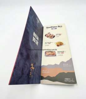 A side-view of the folded brochure, showcasing the internal menu layout, food imagery, and printed text details on a textured blue background A side-view of the folded brochure, showcasing the internal menu layout, food imagery, and printed text details on a textured blue background