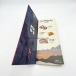 A side-view of the folded brochure, showcasing the internal menu layout, food imagery, and printed text details on a textured blue background